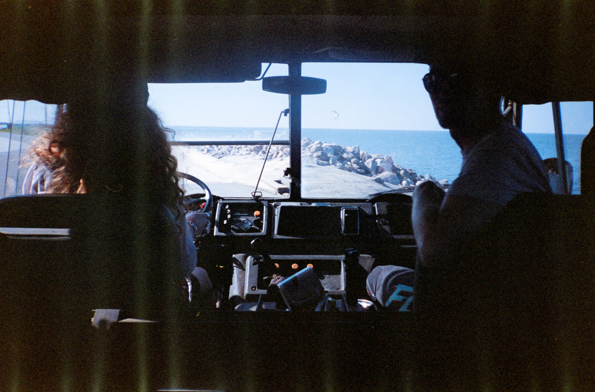 Grainy dark film photo of two people inside a vehicle, taken from pov of backseat