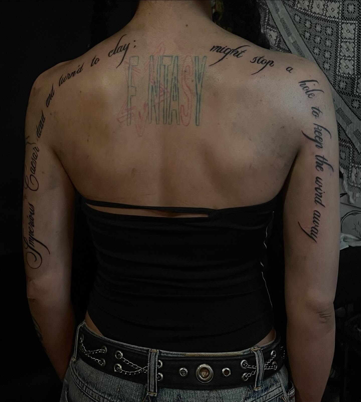 tattoo of a quote in cursive wrapping around arms on the back