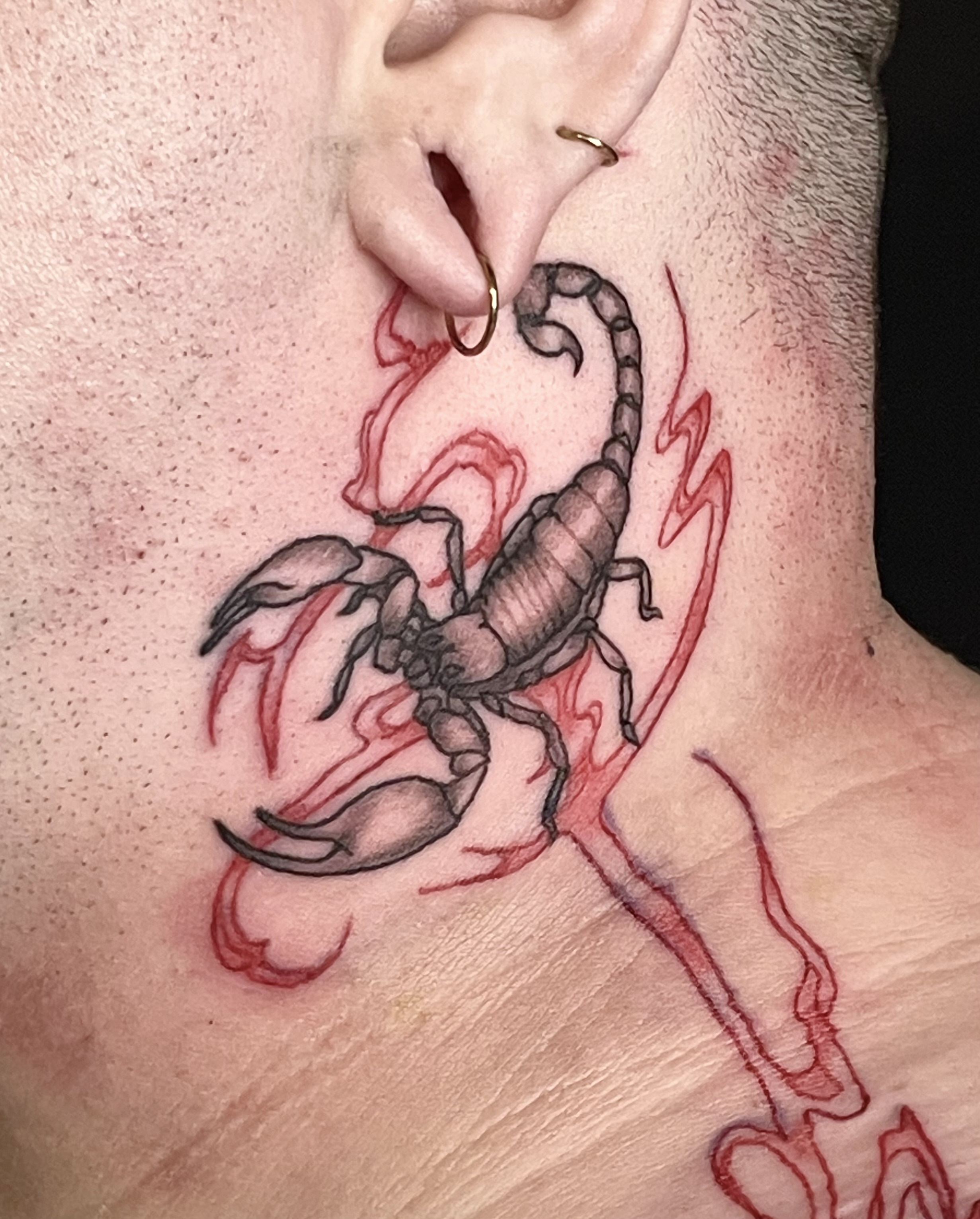 tattoo of a scorpion and red swirling lines on neck and shoulder