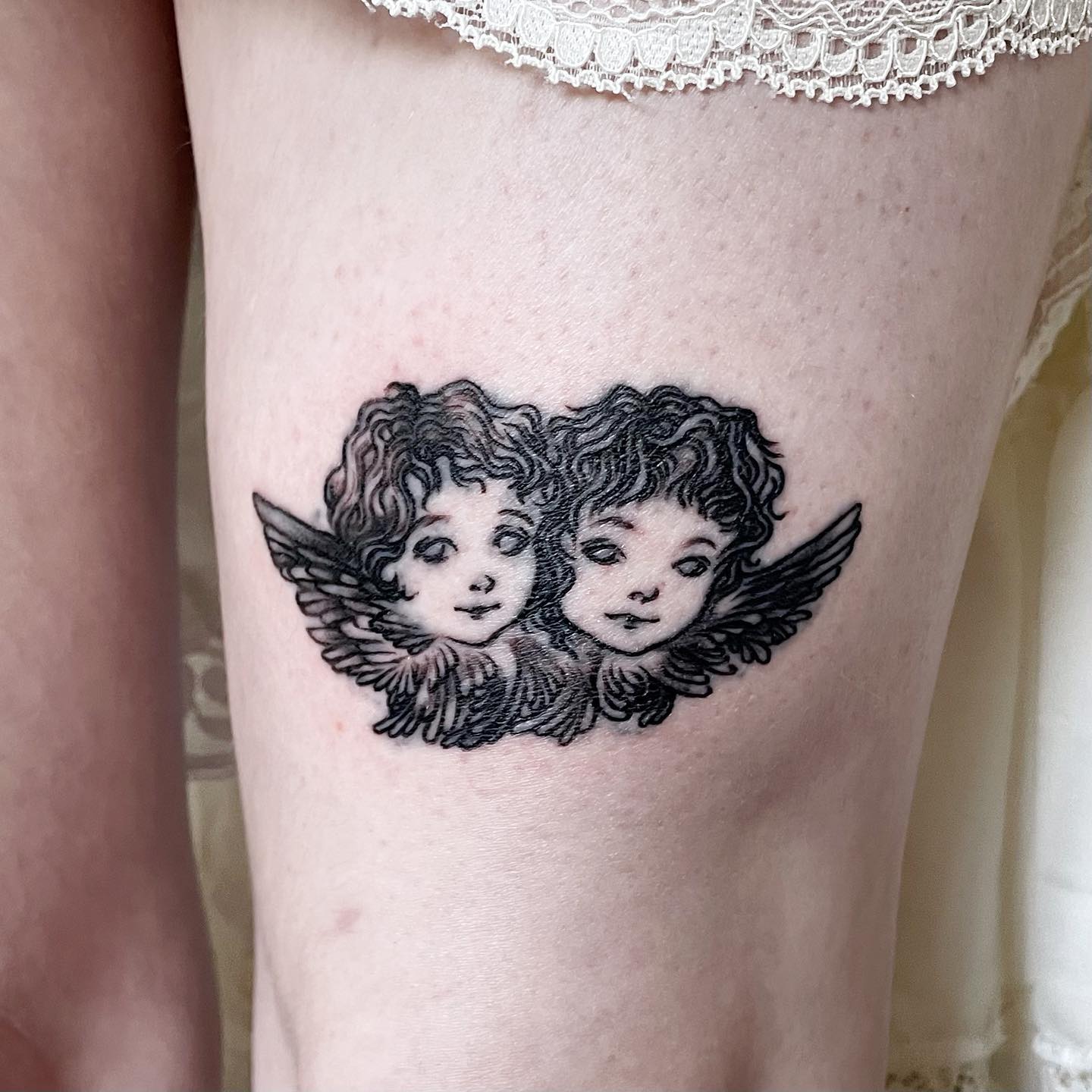 tattoo of two cherub faces surrounded by wings on leg
