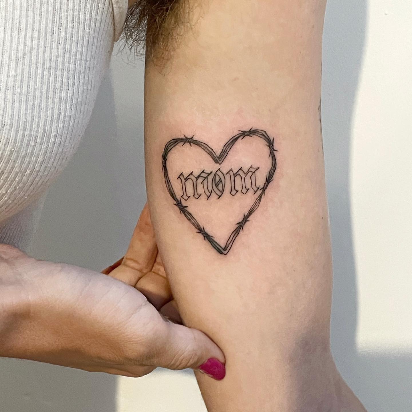 tattoo of a barbed wire heart and mom in gothic letters on arm