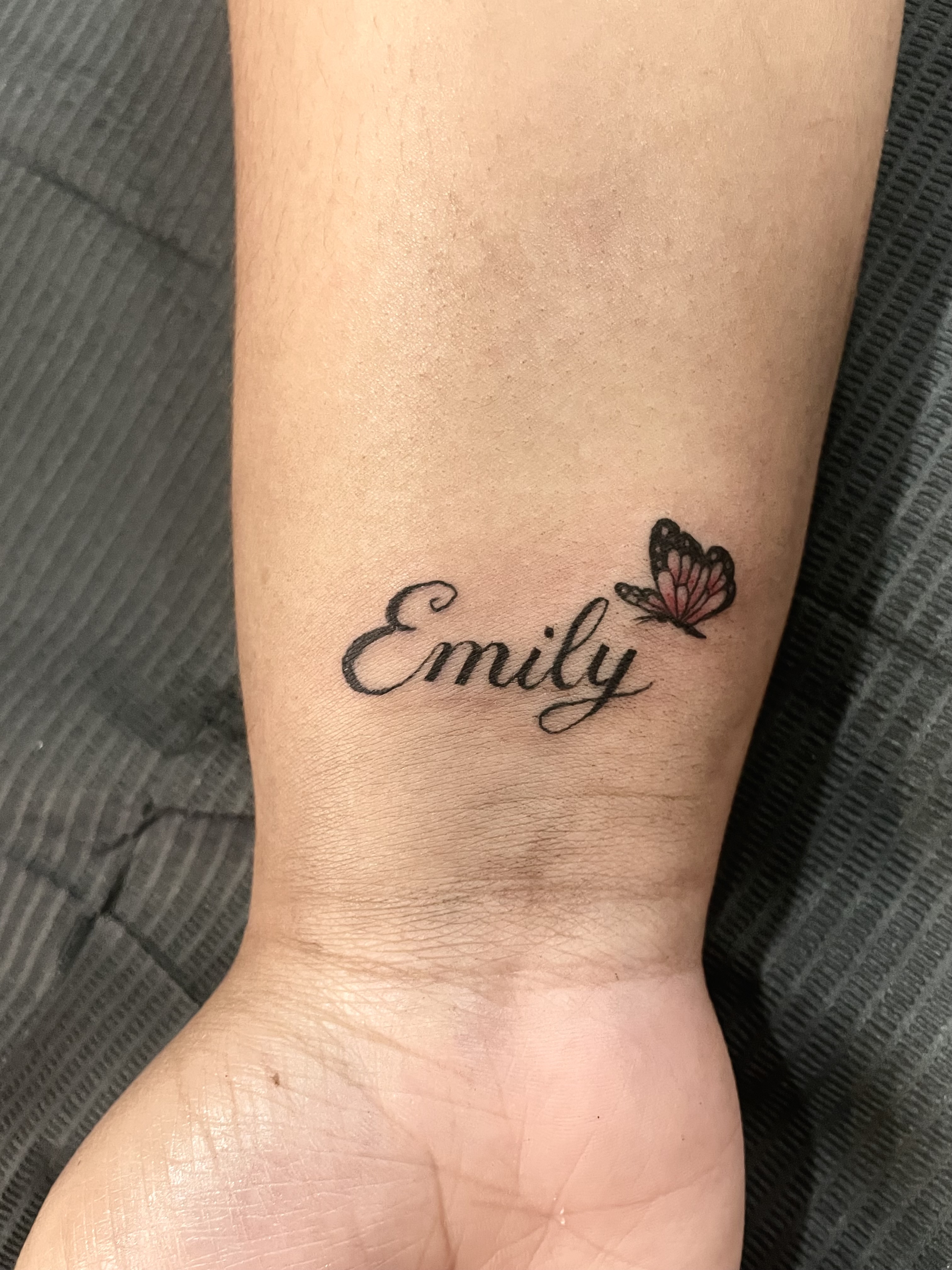 tattoo of the name emily on a wrist with a butterfly