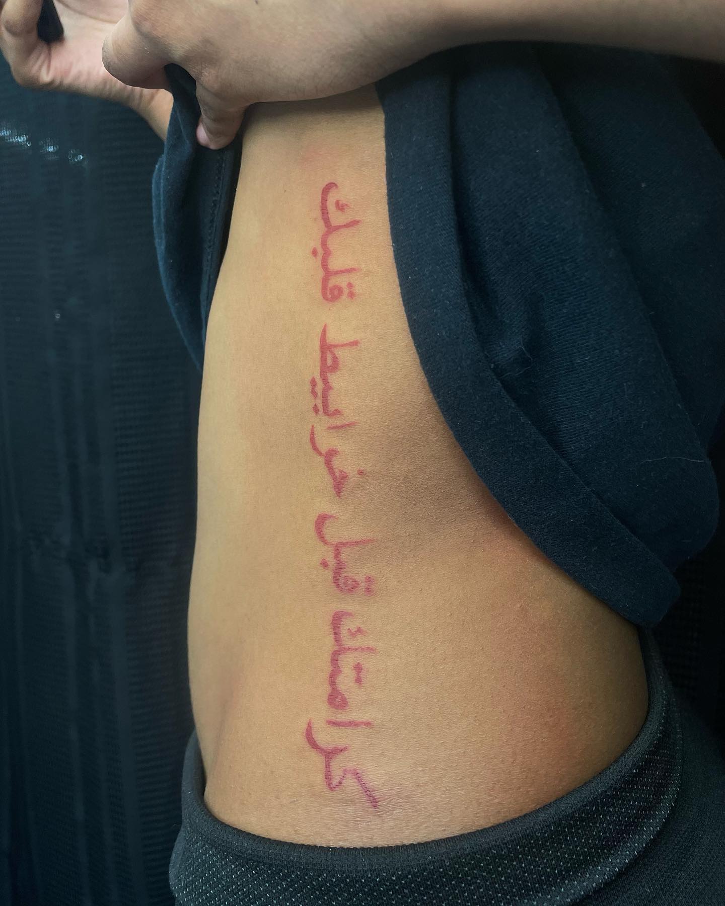 tattoo of red arabic text going down torso